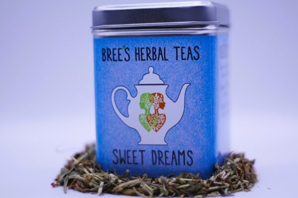 Sweet Dreams sleep tea in a blue tin with herbs around it and a white background